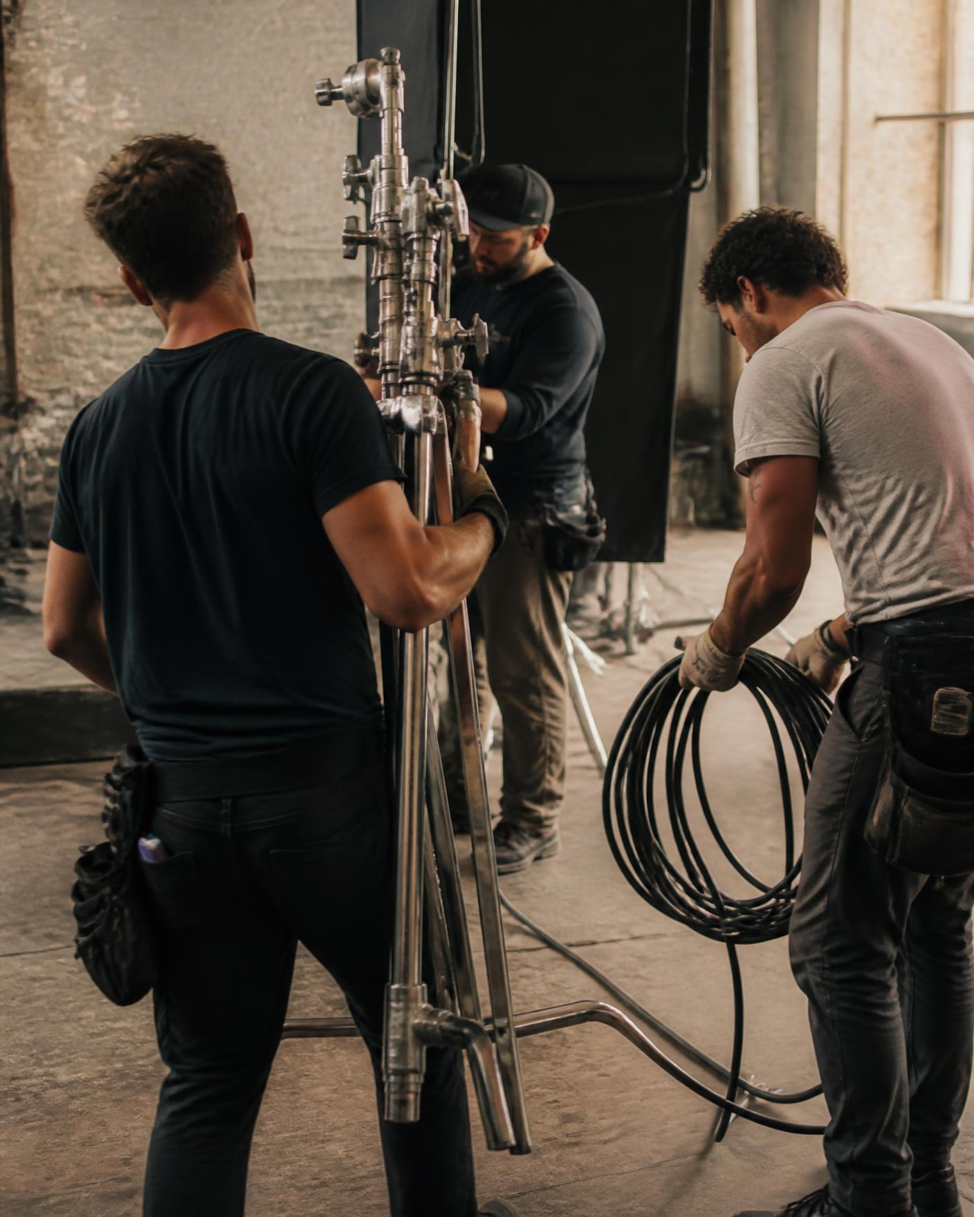 Grip and rigging crew raising a lighting stand and coiling cable on a soundstage